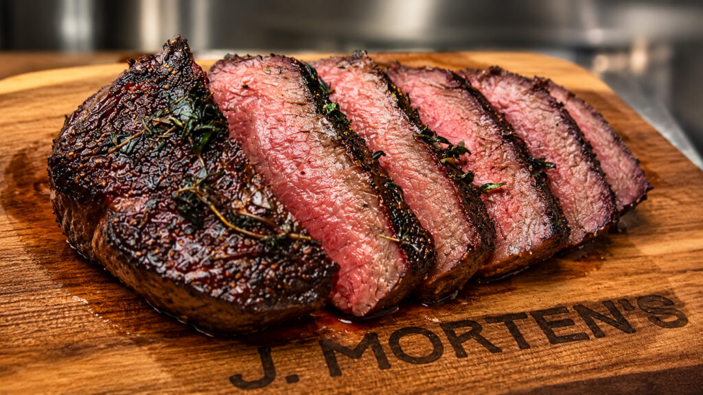 Sliced medium-rare cooked Wagyu steak with a seared herb crust on a J. Morten's wooden cutting board.
