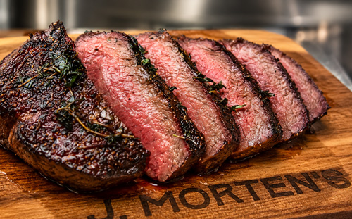 Sliced medium-rare cooked Wagyu steak with a seared herb crust on a J. Morten's wooden cutting board.