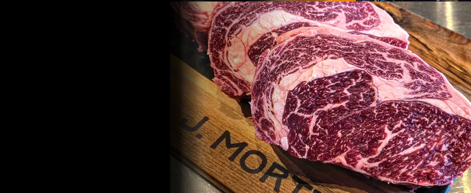 A wide hero banner showcasing premium, heavily marbled raw Wagyu beef steaks on display at a specialty meat market.