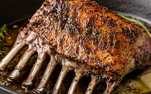 A roasted, golden-brown cooked rack of lamb ready for slicing.