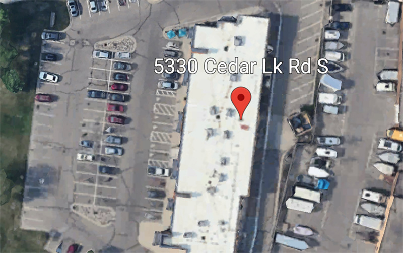 An aerial, birds-eye view of a paved parking lot outside J. Morten's, showing marked stalls, a few parked cars, and clear access points to the storefront.